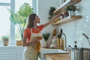 Beautiful young woman dries dishes and putting on kitchen shelf
